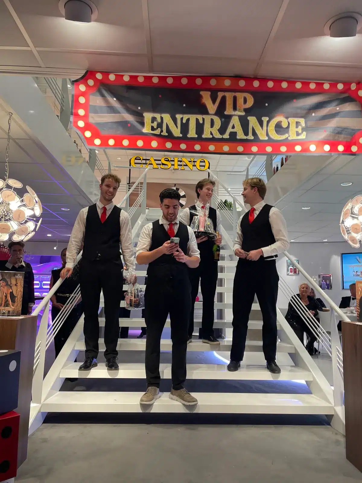 Croupiers van MCN op de verlichte trap onder het VIP Entrance-bord